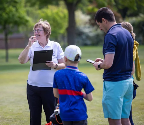 Golf community volunteers speaking with a junior participant outdoors
